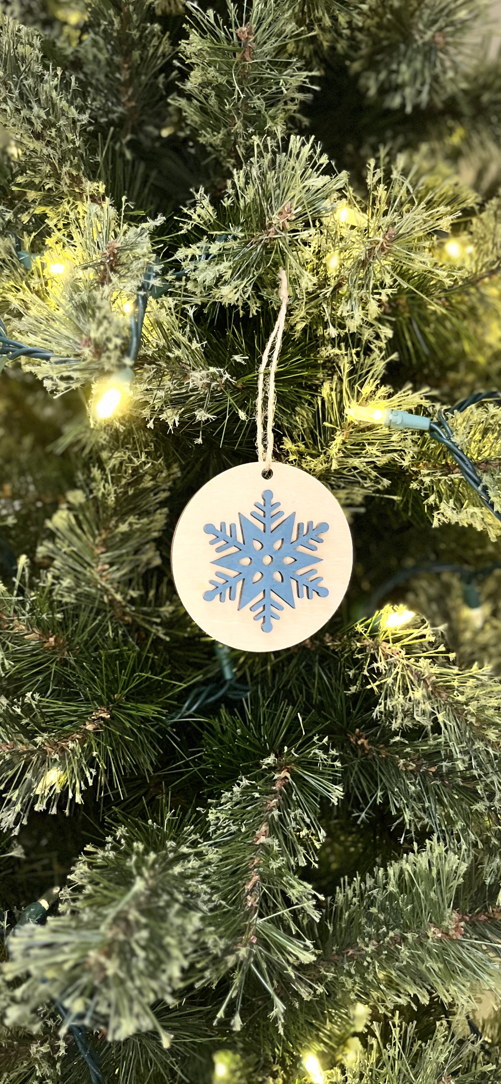Decorative ornament with a snowflake design hanging on a Christmas tree.