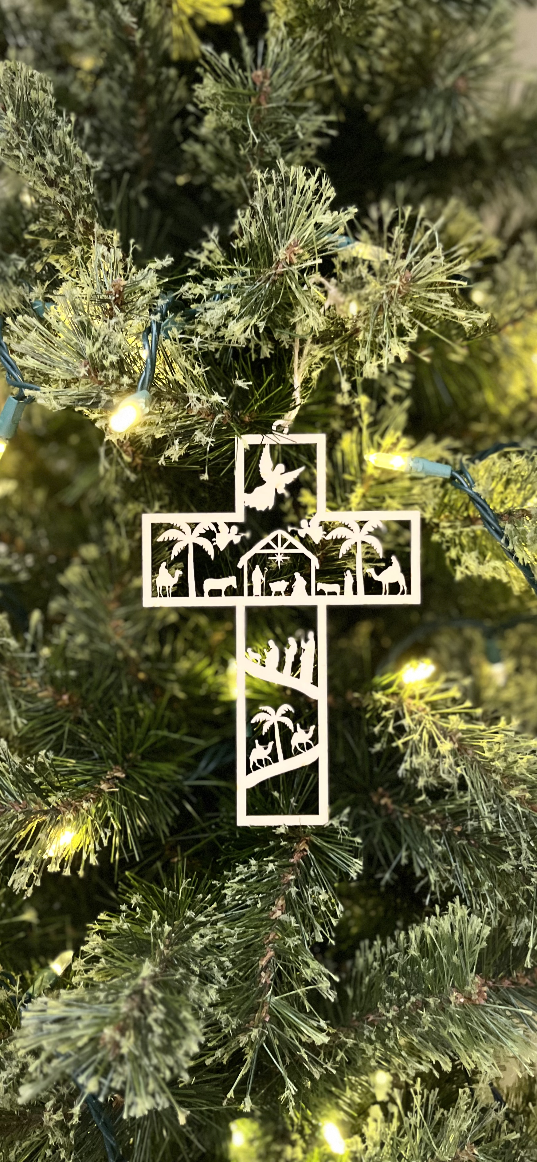 Decorative cross nativity ornament on a Christmas tree with lights