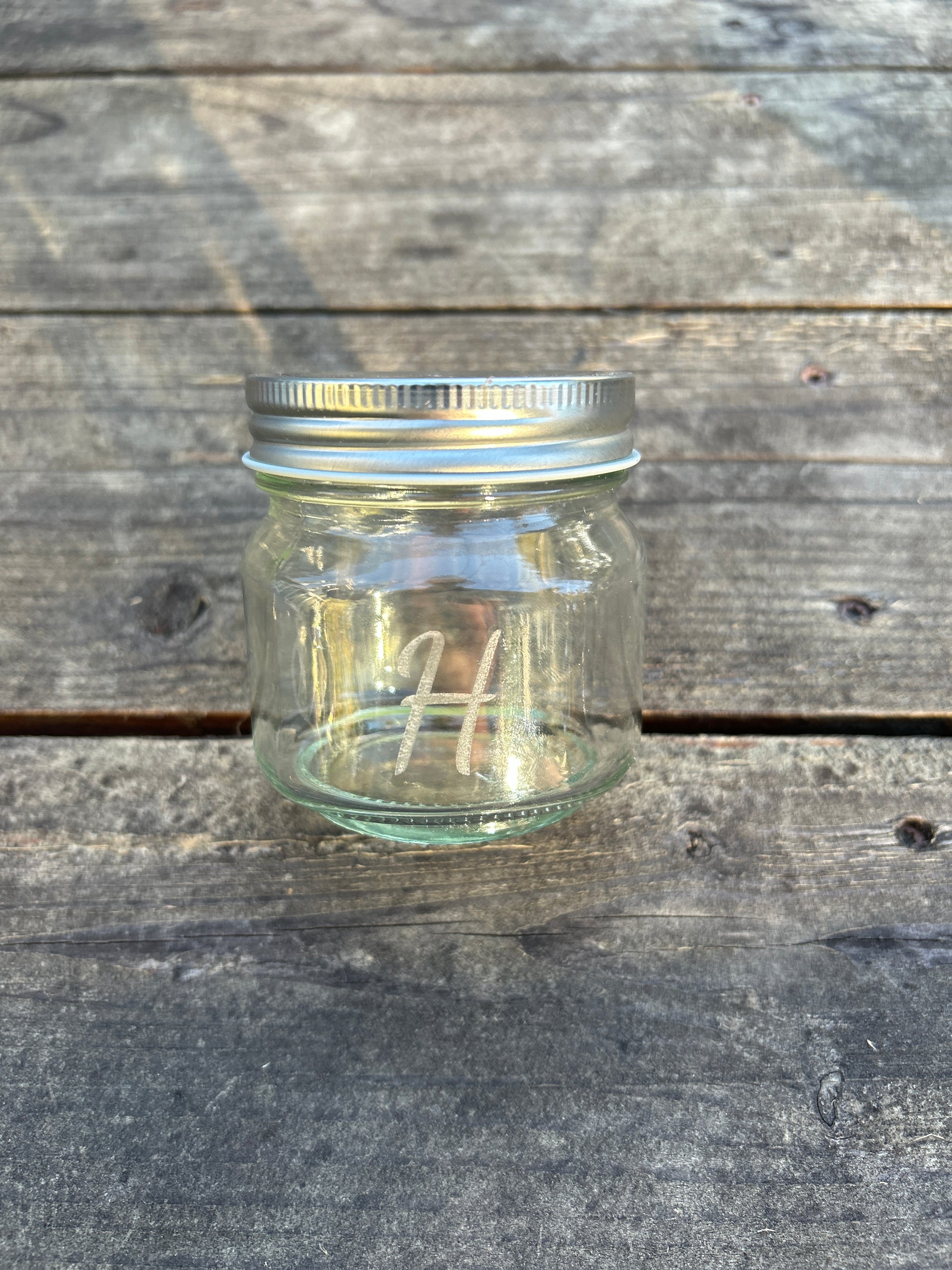 Clear glass jar with metal lid on a wooden surface engraved with initial