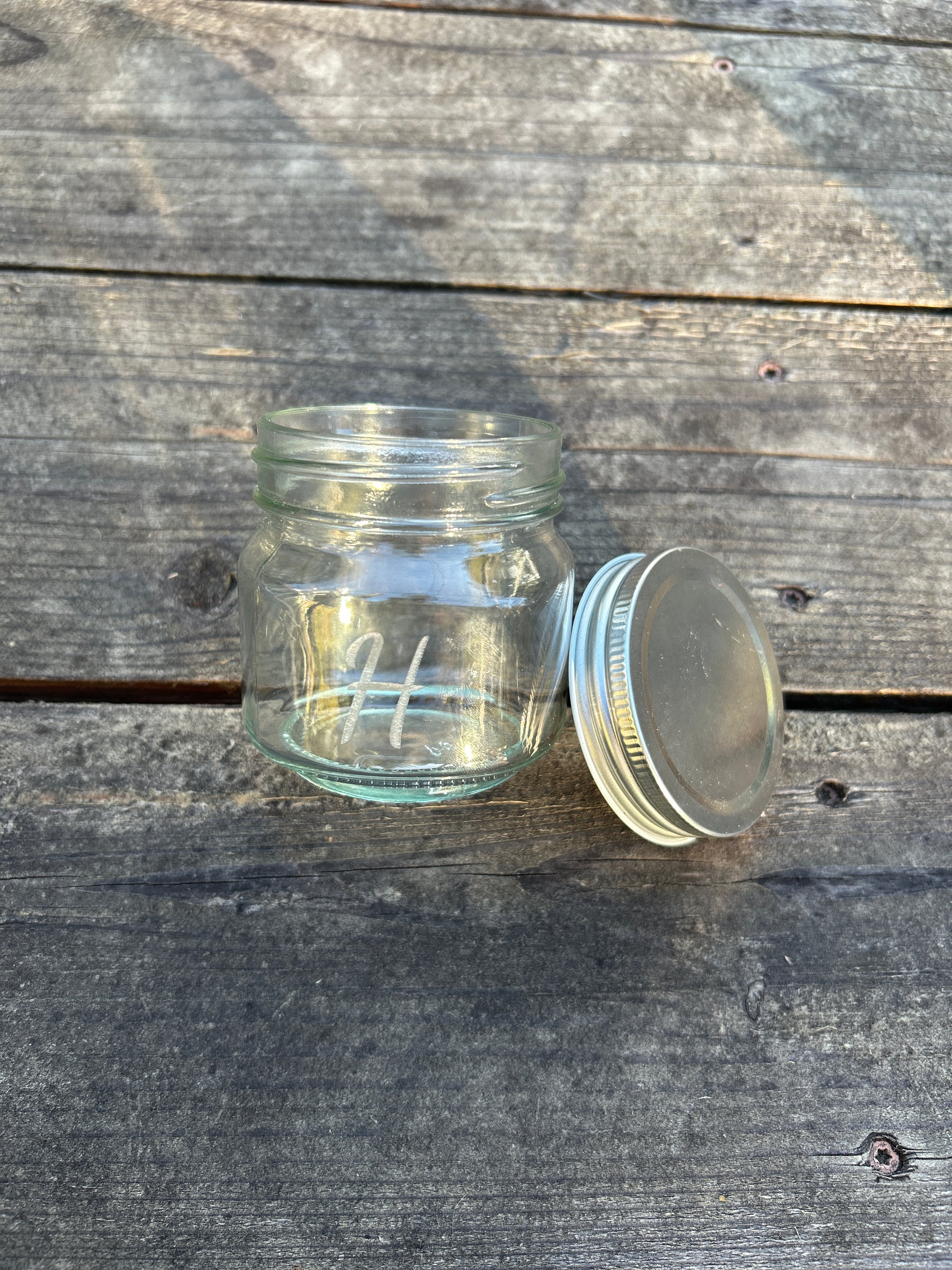 Clear glass jar with metal lid on a wooden surface engraved with initial