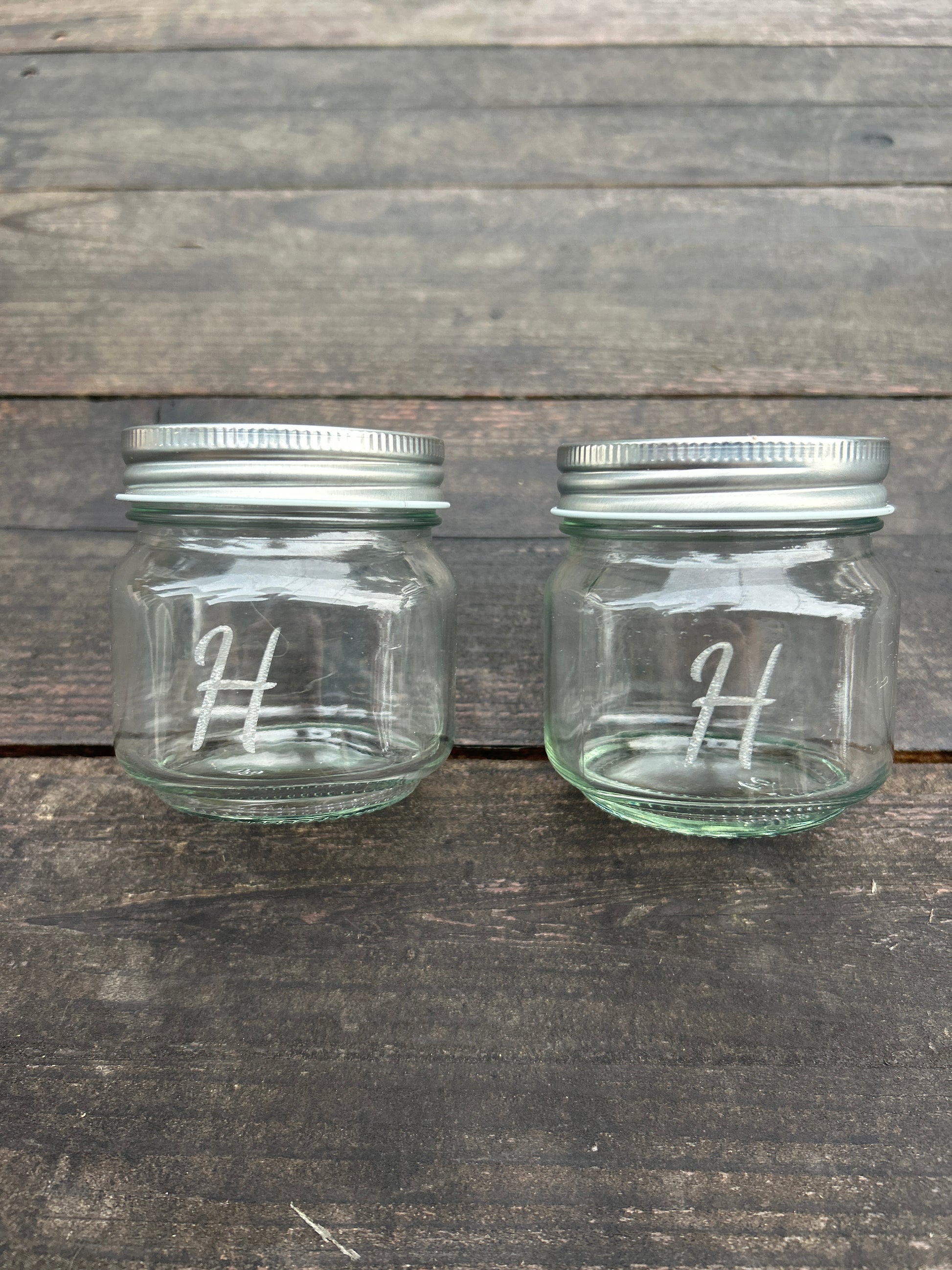 Two custom engraved glass jars with metal lids on a wooden surface