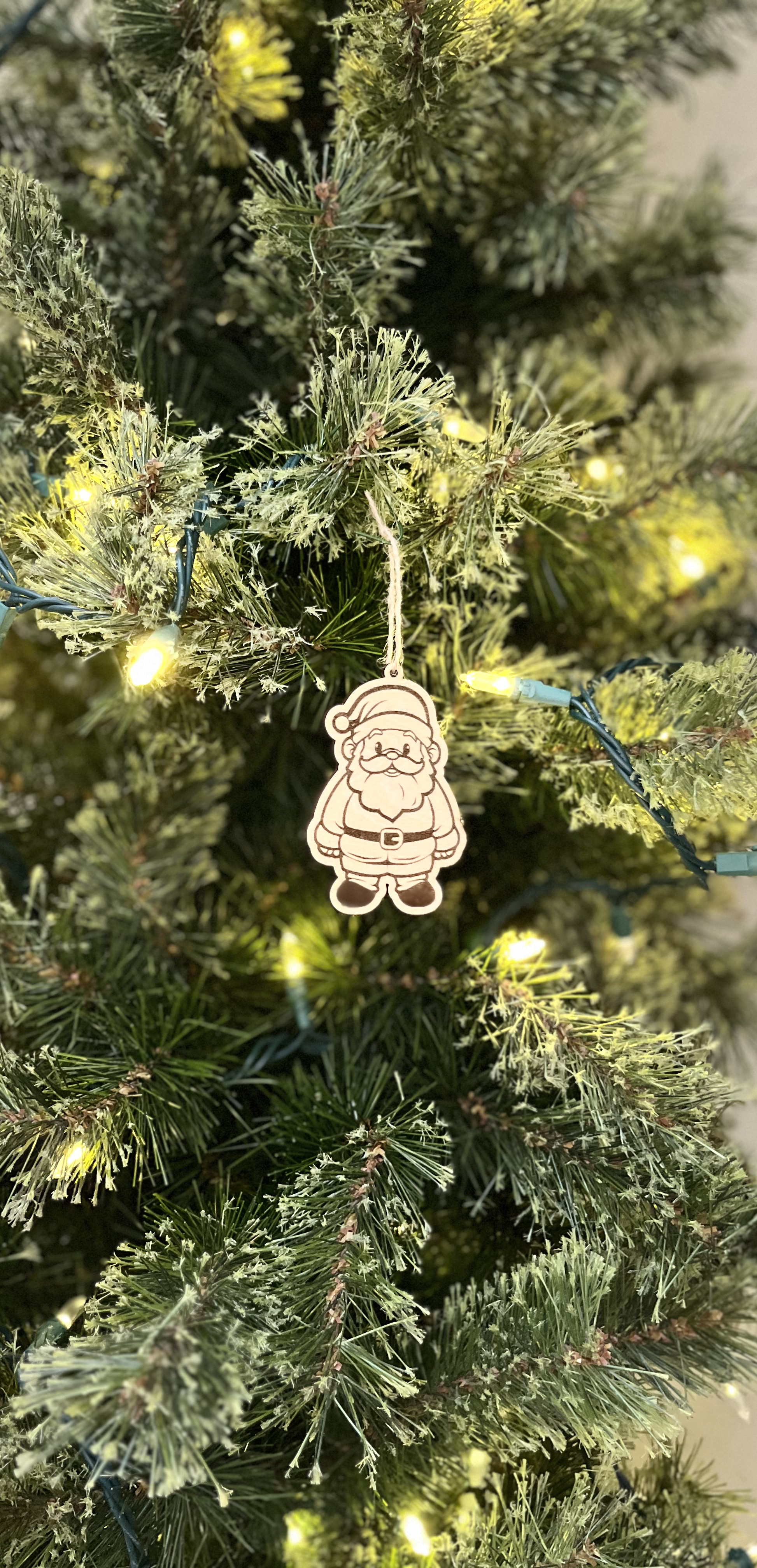 Decorative Santa Claus ornament hanging on a Christmas tree with lights.