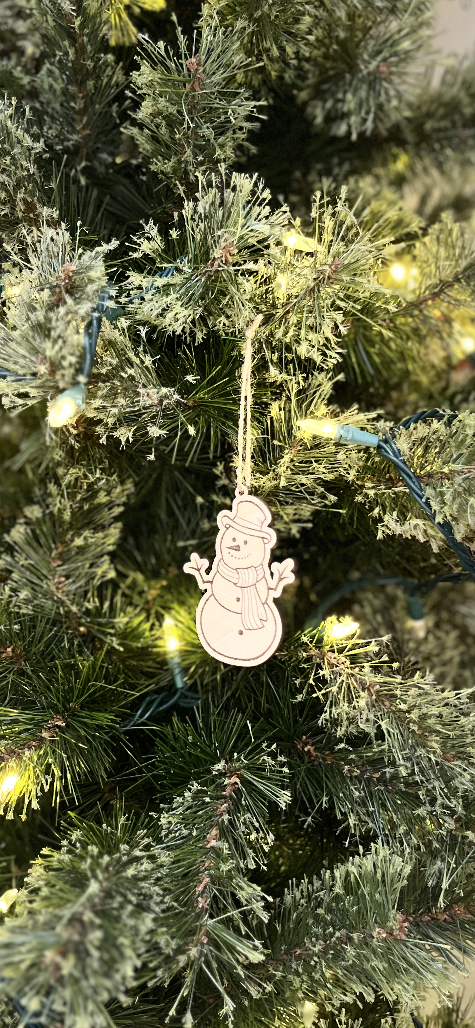 Decorative snowman ornament on a Christmas tree with lights.