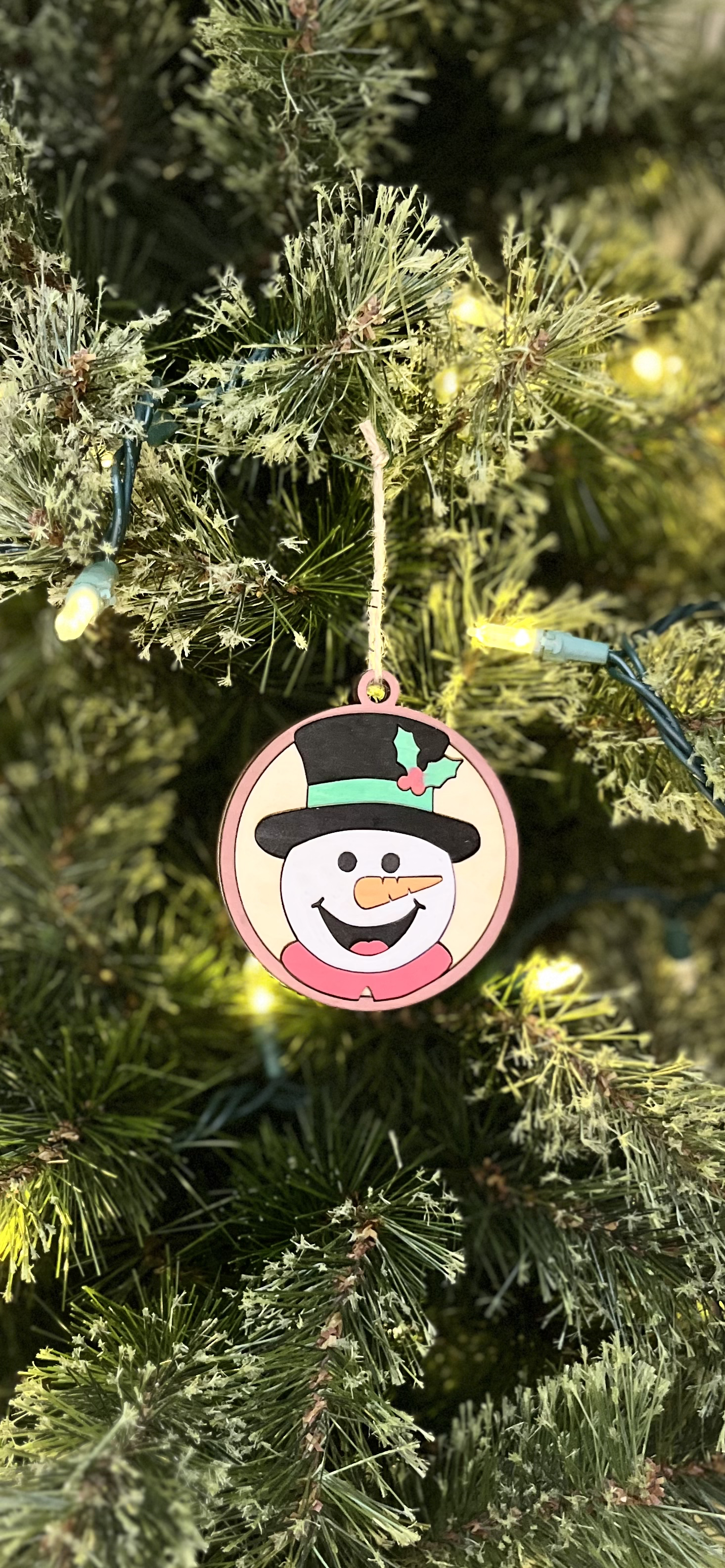 Painted wooden snowman ornament hanging on a Christmas tree