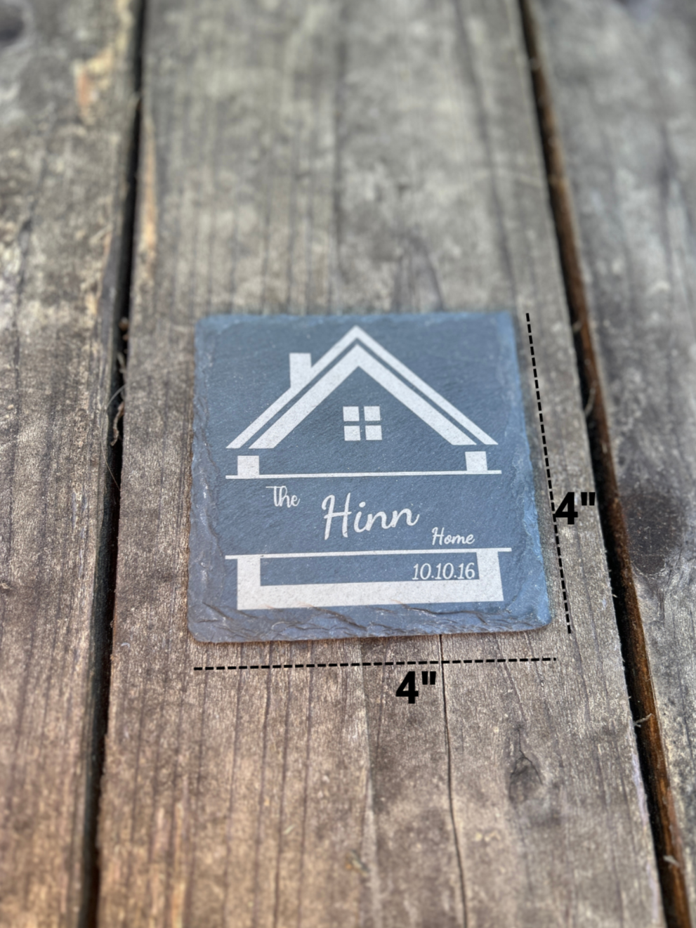 Slate coaster with house design and text on a wooden background